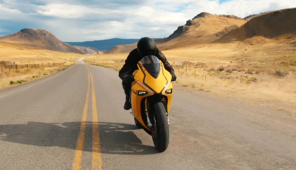 Person in black jumpsuit riding a yellow motorcycle
